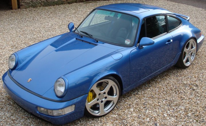 Pistonheads - The image features a Porshe sports car, painted in a vivid shade of blue. The car is positioned on a gravel road, hinting at an outdoor setting. Its wheels, also in silver, contrast with the car's body. The front end of the car, including the hood and bumper, is clearly visible. The Porshe logo, a symbol of the brand's heritage, is also noticeable on the side of the car. The overall scene suggests a moody day, perhaps late afternoon or early morning.