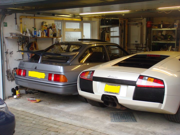 Who has the best Garage on Pistonheads???? - Page 405 - General Gassing - PistonHeads UK - The image features a garage with two sports cars. One car is silver and the other one is yellow, both have large spoilers on the back. They are parked side by side, occupying most of the space in front of the white wall. There are some tools visible, indicating that maintenance or repairs may be taking place. The overall atmosphere suggests a hobbyist's garage, filled with high-performance vehicles and equipment for their care.