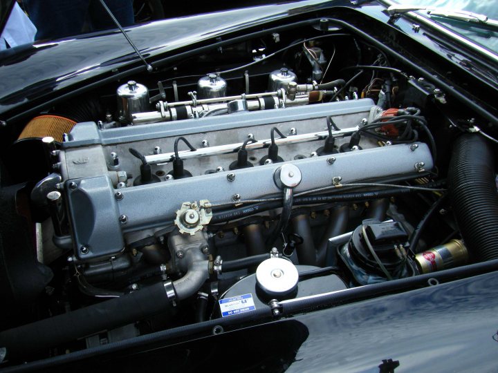 Breakfast Meeting, The Hare, Roxwell 4th June - Page 1 - Kent & Essex - PistonHeads - The image shows the engine and interior cabin of a classic, open-top car. The engine is prominent, with visible components such as the carburetor, intake manifold, and spark plug wires. There are also various other wires and mechanical parts radiating out from the engine bay. The body of the car is black, and there is a person seated in the passenger seat, which is visible through the open roof. The car's headlights and lower exterior panels are also visible, giving a sense of the vehicle's overall aesthetic.