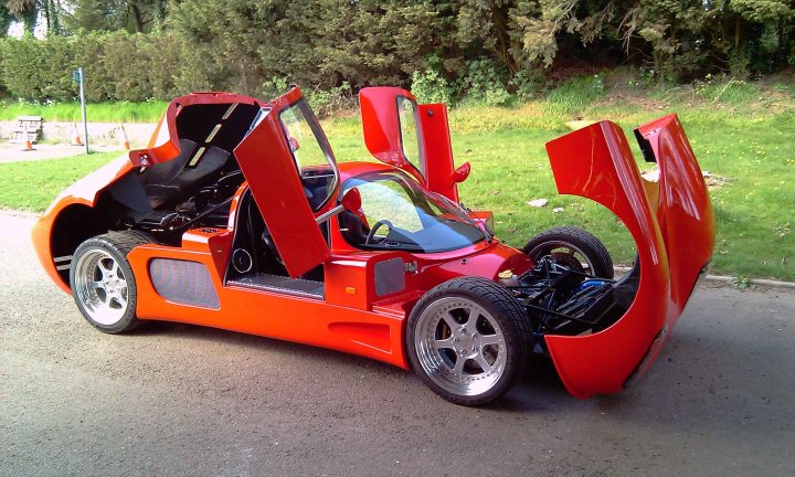 Birth Garage Pistonheads Finally Ultimawell - The image showcases a striking orange sports car, captured in a front three-quarter view. The car's unique features are its two doors, one of which is a gull-wing door that is clearly open. Inside the car, the absence of the roof and one of the two seatbelts gives a sense of the sporty, free-spirited nature of the vehicle. The car is parked on a street, with a lush green lawn visible in the background, suggesting an urban setting.