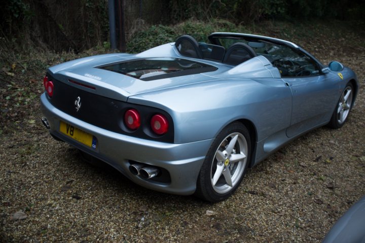 360 thread - Page 1 - Ferrari V8 - PistonHeads - The image showcases a blue Ferrari sports car, parked on a gravel driveway amidst a wooded area. The car is viewed from a front-left angle, with the license plate clearly visible. It features a sleek design with a big spoiler, red taillights, and five-spoke alloy wheels. The vehicle is the center of attention in the middle of the frame, resting against the backdrop of the lush greenery, reinforcing its status as a luxurious, high-performance vehicle.