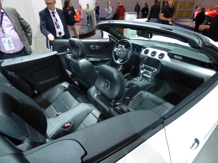 Mustang at IAA Frankfurt motorshow (pic heavy) - Page 1 - Mustangs - PistonHeads - The image features a convertible car showcased at what seems to be an auto show or exhibition. The car is well-polished and shines brightly under the showroom lighting. The cockpit of the car is visible, displaying a dashboard with gauges and controls. The car has its top up and is parked among other presenting vehicles. Congested with people walking, interacting, and filling the background, the image captures the lively atmosphere of a car show.