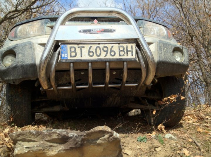 Pistonheads - The image shows the front view of a dirty vehicle, likely an SUV, parked on an off-road trail with bare tree branches in the foreground. The vehicle has a large grille design and the registration number 'BT 6909 BH', along with some design accents, indicating it may be a specific model. The tires appear to be off-road or all-terrain types, suggesting this vehicle is designed for off-road conditions.