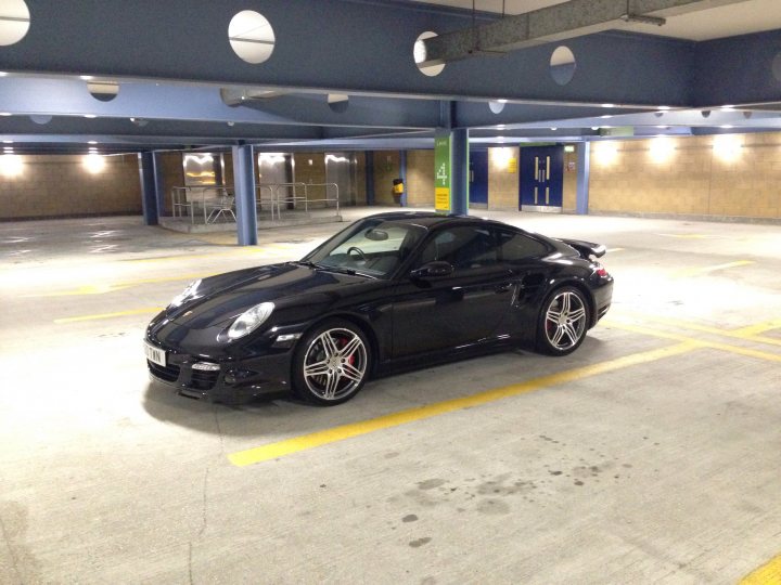 997 Turbo Gen 1 prospective purchase which colour  - Page 5 - 911/Carrera GT - PistonHeads - The image showcases a black 3.6 liter Biturbo Porsche 911 GT2 RS sports car elegantly parked inside a spacious and spotless garage. The car is positioned in the middle of the frame, its sleek lines and polished surfaces reflecting the bright lights that illuminate the surrounding area. The garage itself is characterized by a blue ceiling and concrete floor, providing a stark yet stylish contrast to the car's shiny exterior. The far end of the garage reveals a row of similar cars, all identical in color and design, suggesting a passion for luxury vehicles.