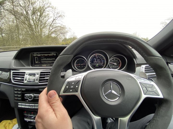 Mercedes E63 AMG wagon - Page 1 - Readers' Cars - PistonHeads - The image showcases the interior of a Mercedes-Benz car. A person is seated in the driver's seat, holding a key with the Mercedes emblem. The steering wheel is prominently displayed, featuring the brand's logo and various control buttons. The dashboard houses several digital screens displaying vehicle information such as speed and fuel level. The overall setting suggests that the car is either parked or stationary in an outdoor environment.