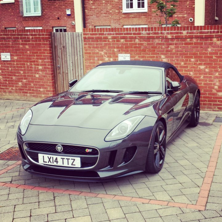 Proud first Jag Owner - Page 1 - Jaguar - PistonHeads - The image shows a sleek, black sports car parked on the street in front of a tall, red brick building. The vehicle's glossy finish reflects the residential area around it. Adjacent to the car, there is a brick wall with a gate, and to the right, there's a small, red-brick building with a window. The car bears the license plate "LX14 TTZ." The texture of the brick road provides a patterned backdrop to the car.