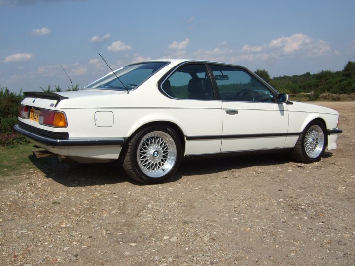 Csi Chimaera Tvr Pistonheads - The image displays a white BMW 8-series, which can be identified by its distinctive long wheelbase and aerodynamic shape. The car is parked on a dirt ground, facing towards the left side of the image, with the front of the vehicle visible. The vehicle is equipped with a clear windshield and a black rear spoiler, accentuating its sleek design. The photo seems to have been taken during the day under clear skies, with a backdrop that includes an expansive sky and minimal ground vegetation.