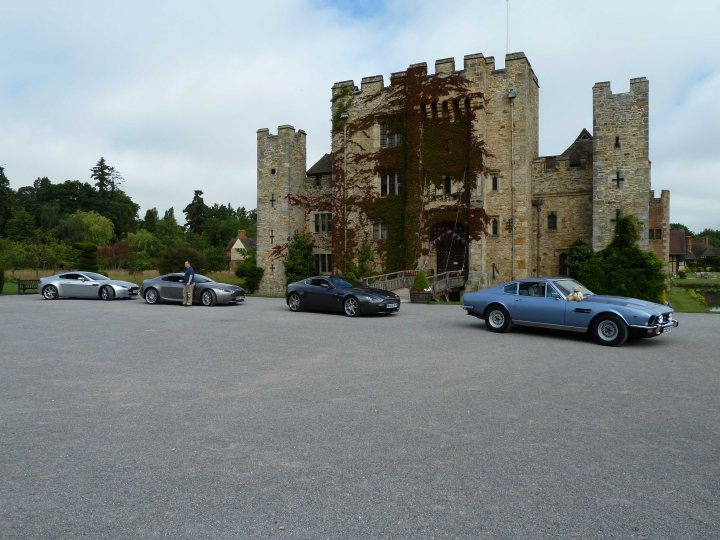 hever pics - Page 1 - Aston Martin - PistonHeads - The image showcases an outdoor scene where four classic cars are neatly parked around a circular driveway. Two of the cars are silver, while the other two are painted in a vibrant shade of blue. In the background, a large, medieval-style building with battlements and a red roof stands out prominently. The sky is clear, suggesting that the photo was taken on a bright day. The setting appears to be in the countryside or a park, as no urban buildings are visible in the vicinity.