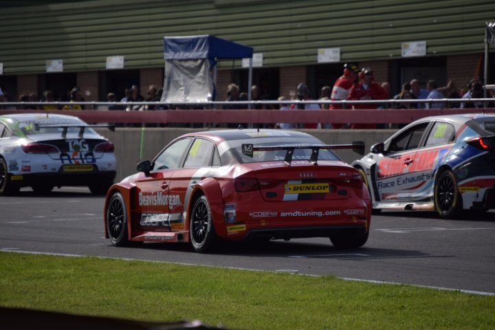 BTCC - Snetterton - Rounds 16, 17, 18 - Page 2 - General Motorsport - PistonHeads - The image is a dynamic racing scene with several cars on a race track. In the foreground, a red car with a white number 30 is taking a sharp left turn. There are other cars behind it, suggesting they are also participating in the race. The atmosphere is focused and competitive, indicative of a professional racing event. The track is surrounded by a grassy area, and there are several spectators visible on a bridge above the rapping, possibly cheering for the racers. The quality of the image, particularly the blurring of the background, emphasizes the high speed of the cars.