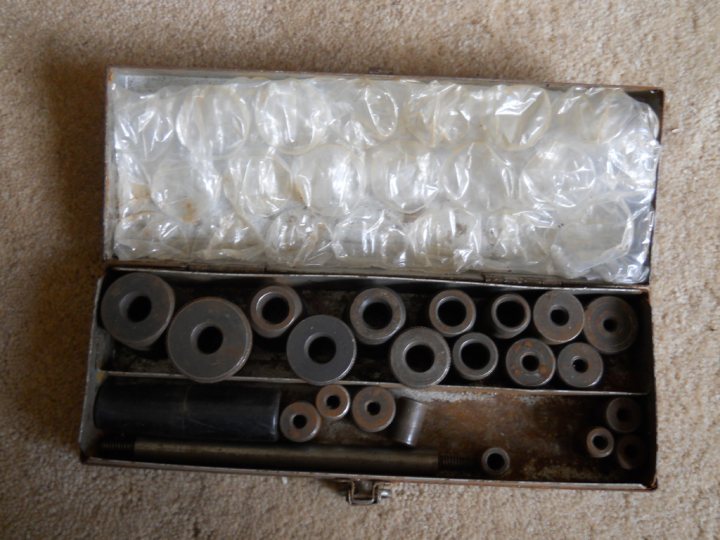 Name this tool! - Page 1 - Home Mechanics - PistonHeads - The image shows an open suitcase lying on a light-colored carpet. Inside the suitcase, there are two main sections. The top section is mostly covered with clear, plastic bubble wrap. Below it, the bottom section is divided into numerous compartments, each containing several metal rings. The metal rings have a similar appearance but are secured within the containers. The suitcase's handle is visible on the left side, indicating it is ready for travel or transport. There is no text or branding visible in the image. The style of the image is a simple, direct photograph without any filters or artistic effects.