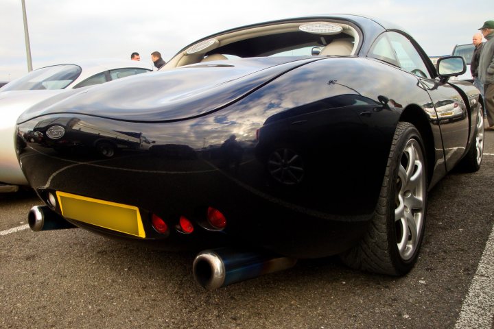 Pistonheads Oxford Sunday Service - The image showcases a sleek, black sports car parked in a lot. Its elegant design and glossy finish reflect the soft lighting of a cloudy day. Limited to three visible windows, the car's design emphasizes aerodynamics, a characteristic often found in sports vehicles. The exhaust pipes jutting out from the car suggest its powerful and high-performance nature. In the background, other cars are parked, adding to the ambiance of the scene. The overall image gives a sense of luxury and speed.