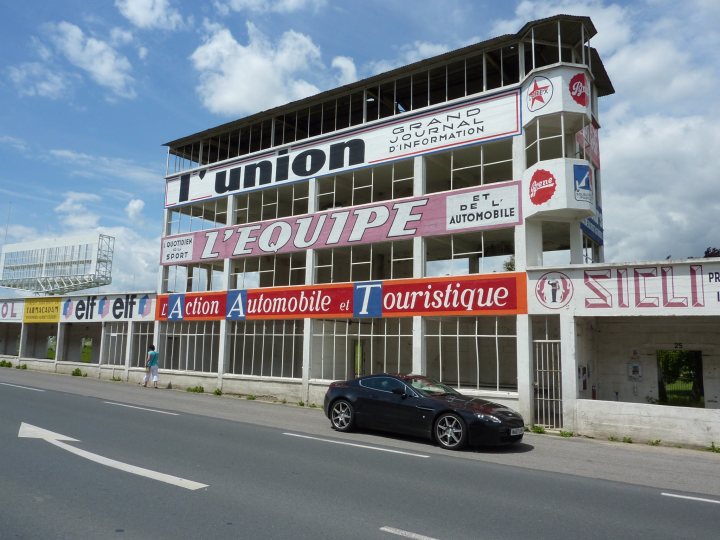 French trip - Page 1 - Aston Martin - PistonHeads - The image features a car dealership located on a street corner next to a racetrack. The dealership is notable for its three-tiered building, prominently displaying an advertisement for "L'equipe Automobile et Touristique." There are several signs and banners, and above the main entrance, the sign "UNION" is visible, indicating that this is the union building for the "Grand Prix Dynasty / Information." Additionally, the dealership is located near the "SIDE Rosalie," a region or landmark within the context of the racetrack.