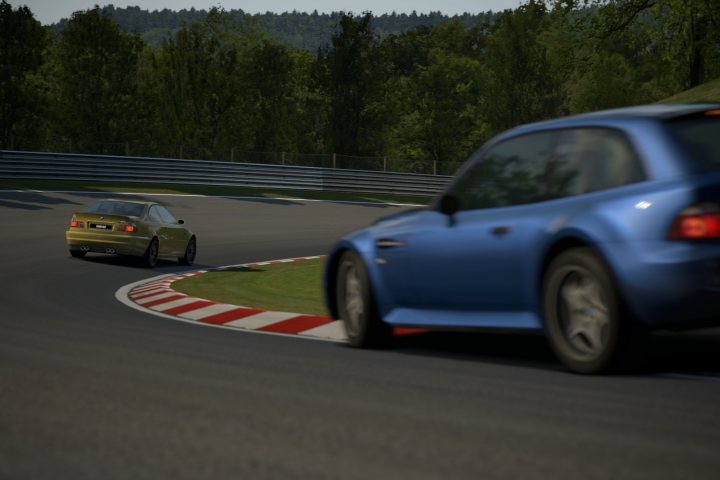 Gran Turismo 6 picture thread - Page 4 - Video Games - PistonHeads - This image captures a moment on a winding, grass-lined road that appears to be part of a racing track. A blue sports car is in the foreground, leaning into a turn, with its headlights illuminated and the driver presumably skillfully navigating the curve. Behind the sports car is a yellow sedan, which is racing or chasing the sports car, exhibiting a notable difference in speed and agility relative to its green counterpart. The environment is lush with trees in the background, underlining the tranquil setting, in stark contrast to the intense racing action taking place on the track.