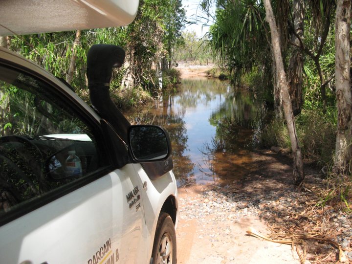 A car is parked on the side of the road - Pistonheads - The image captures a scene of adventure, featuring a white truck parked at the edge of a rugged, muddy trail. The truck, with a spare tire attached to its back, is angled towards us, showcasing its sturdy design and suggesting recent use in this natural setting. The trail, enveloped by lush trees, leads the eye towards a serene body of water that reflects the distant horizon. The mood is one of anticipation for a journey beyond the confines of the captured frame.