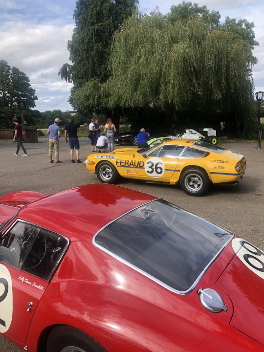 So what have you done with your Aston today? (Vol. 2) - Page 105 - Aston Martin - PistonHeads UK - The image shows a scene in a parking lot where two vintage sports cars are parked side by side. One car is red, while the other is yellow with black stripes. Both cars have numbers and sponsorship logos, indicating they may be part of a racing event or series. In the background, there is a person standing near the cars, possibly an attendee or staff member. The setting suggests that this could be a race track or a similar venue dedicated to vintage vehicles.