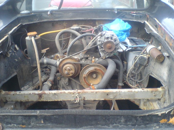 Jps Europa Pistonheads - The image shows the engine bay of a vehicle with its body removed, exposing the rusty and well-used internal mechanisms. The engine, of a small size, has several visible functions, with hoses and belts routing to various parts. The vehicle appears to be on a repair or restoration process, given the bareness and seemingly mechanical nature of the scene. The rust and absence of a car body indicate the state of disuse or possible abandonment of the vehicle. The perspective of the image suggests it was taken from outside, perhaps by a professional involved in the restoration process.