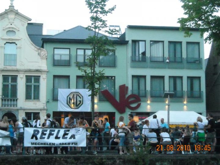 Pistonheads - The image depicts a lively urban scene with a large gathering of people. There is a crowd, predominantly consisting of young individuals, standing in line in front of a building with a white sign saying "REFLEX". The building has a modern architectural style with a green facade. There is also a white awning with a sign that says "MOTOM", which indicates it might be a store or a place associated with motorcycles. The photo is timestamped on the bottom right corner, suggesting it was taken at 21:08 on August 8, 2010. The timestamp shows the date and the time, providing a record of when the image was captured.