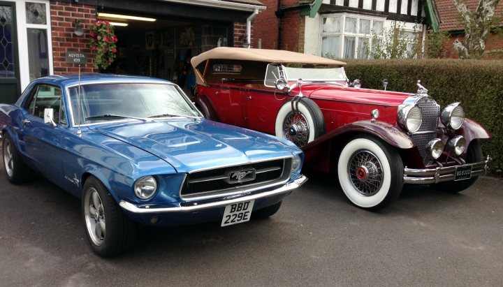 1967 / 68 Mustang wanted - Page 1 - Mustangs - PistonHeads - The image showcases a peaceful driveway scene featuring two classic cars parked next to each other. The blue car, which is a Mustang model, has a vibrant and shiny appearance suggesting it's well-maintained. Beside it, a red classic car, presumably a Rolls Royce, shares the spotlight.

The vehicles are parked in front of a quaint front house that has a charming brick wall, adding to the vintage aesthetic of the setting. The house is tall and flat, featuring a canopy that extends outward, possibly providing shade to the house's front.

The house is nestled amidst a tree-lined street, affirming the serene and tranquil atmosphere of the scene. The overall composition of the image paints a picture of a calm family home on a quiet day.