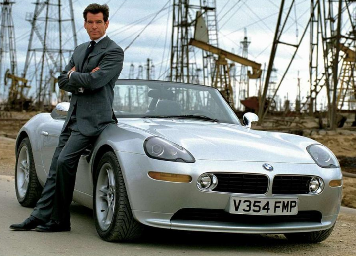 RE: BMW Z8: Spotted - Page 3 - General Gassing - PistonHeads - In the image, we see actor Pierce Brosnan, known for his roles in iconic movies and television series, posing confidently next to a silver BMW. He is dressed in a classic black suit and tie, perfectly complementing the sleek car. The setting is intriguing, with an oil rig visible in the background, suggesting a theme of power and luxury. The blue sky forms a serene backdrop, adding an air of success to the overall scene.