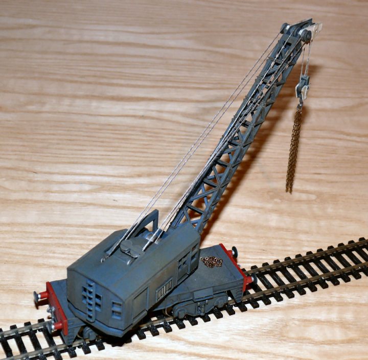 Pistonheads Dapolairfix Hooo Crane Tonne - The image features a miniature size model of a construction crane situated on a train track set against a wooden surface. The crane is painted in a dark blue color, and its boom is extended outwards, giving it a prominent and extended appearance. The train track, which appears to be in the 0 gauge scale, runs horizontally across the surface. In the upper right corner of the image, a small end of a laptop or monitor can be seen.