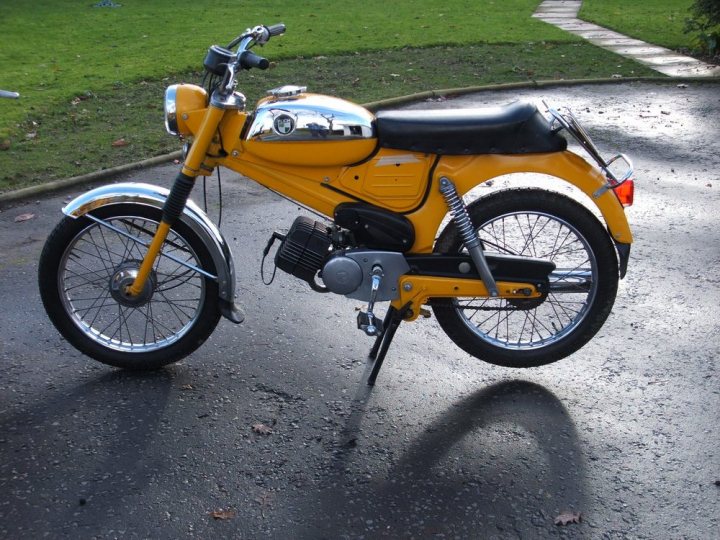 Mopeds from the 70s - Page 1 - Biker Banter - PistonHeads - The image features a vintage yellow motorcycle parked on a driveway. Another bike is visible in the background. The motorcycle has orange fenders and black seat. It also appears to have metallic components, contributing to its distinctive, old-fashioned aesthetic. The precise location or conduct of activities related to the motorcycle cannot be determined from the image alone.