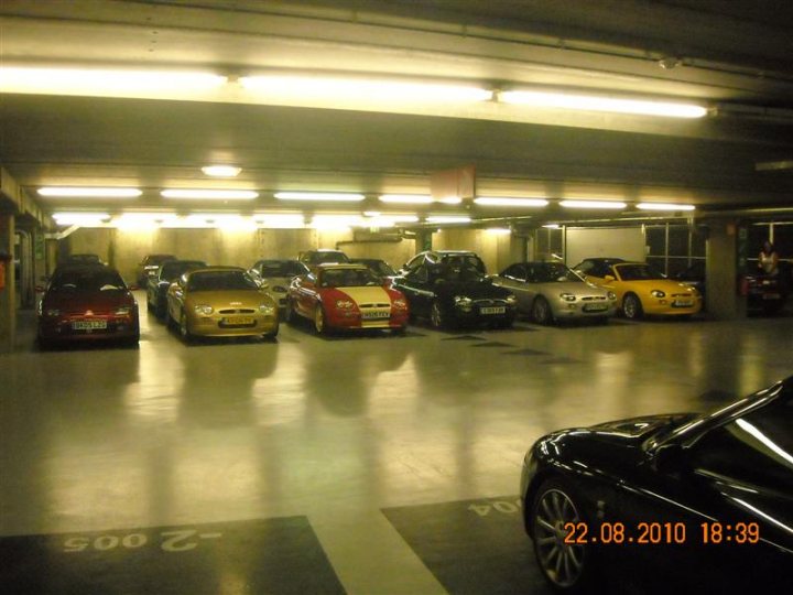 Pistonheads - The image shows a parking garage interior, with a row of cars parked parallel to each other. The environment suggests an underground setting with yellow lighting and clearly marked parking spots. The garage is constructed with concrete pillars and a high ceiling. The date on the image indicates it was taken on August 22, 2010, at 18:39.