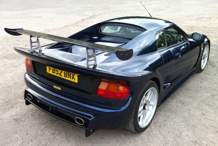 Any one owned fb52 bnx - Page 1 - Noble - PistonHeads - In the image, a black sports car is parked on a concrete surface, with its rear end in the frame. The most striking feature of the car is its large wing spoiler, attached to the top of the trunk. The license plate of the car is visible and reads "F456 BXN". The car is equipped with chrome rims that shimmer in the light. The car's sleek design and the wing spoiler suggest it might be a high-performance model.