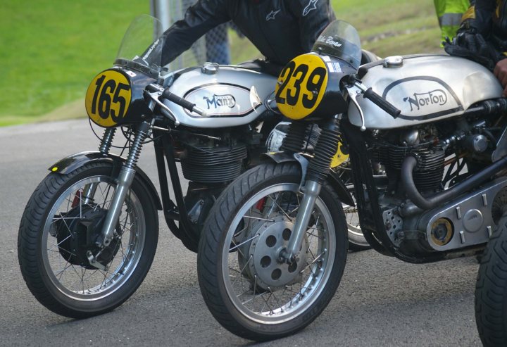 Vintage Motorcycle Club race pic's - Cadwell - pic heavy! - Page 1 - Biker Banter - PistonHeads - The image showcases two beautifully detailed motorcycles parked side by side. The motorcycles are white and adorned with black and yellow numbers on the front. The larger number is 165, while the smaller number is 339. The motorcycles are stationed on the asphalt, and the person wearing a helmet in the background suggests that they might be the owners or riders. The scene evokes a sense of anticipation and adventure, typical of a race track or a motorcycle event.