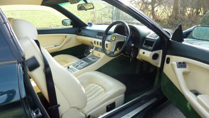 RE: You Know You Want To: &#163;17K Ferrari 456  - Page 14 - General Gassing - PistonHeads - The image showcases the interior of an older car, viewed from a seat in the left side door. The car features plush white leather seats and a green console armrest. The dashboard is adorned with a variety of gauges and indicators, indicative of the vehicle's era. The steering wheel, positioned in the center of the car, adds to the vintage aesthetic. Amazingly, the car appears to be in pristine condition despite its age. The image does not contain any visible text or texts that are legible. The background through the open driver's door window reveals a lush green field under a clear sky, providing a serene backdrop to this atmospheric view.