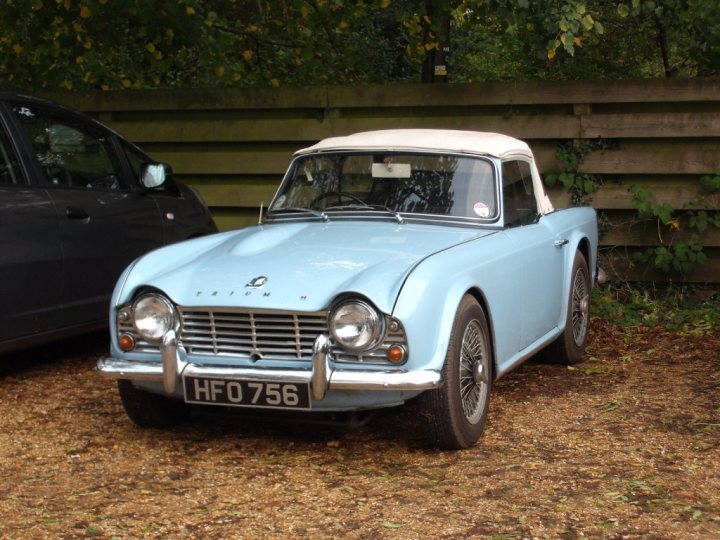 COOL CLASSIC CAR SPOTTERS POST!!! - Page 475 - Classic Cars and Yesterday's Heroes - PistonHeads - The image shows a blue vintage car parked on a gravel surface. The car, with white text on the grill, has a classic design featuring two round headlights and a compact body. In the background, a black car is visible to the left side of the image, suggesting a comparative size between the two vehicles. The setting seems to be a private or outdoor parking area, possibly by a roadside given the size of the vehicles and the presence of gravel.