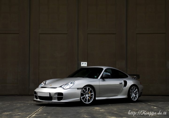 A car is parked in front of a parking meter - Pistonheads - The image features a silver sports car situated in front of a brown, wooden wall. The car is captured from a side angle, showcasing its sleek lines and distinctive rear spoiler. Its metallic silver finish contrasts with the warm tones of the brick wall. The ground appears to be made of concrete, which complements the hard, edgy design of the car. There are no visible texts or other objects in the image.