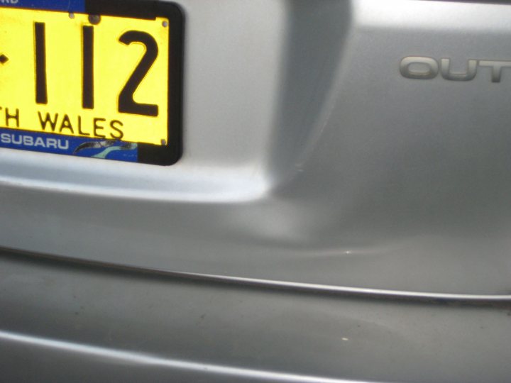 Pistonheads - The image features the rear of a car, focusing on the license plate area. The license plate is prominently displayed, showing the registration number "W12". Above this, there is a representation of a green landscape, most likely representing West Wales, and the word "Subaru". The style of the image is realistic and is possibly intended to provide information about a specific model or region associated with this vehicle. The metallic texture of the car's surface reflects light, indicating a shiny, polished appearance.