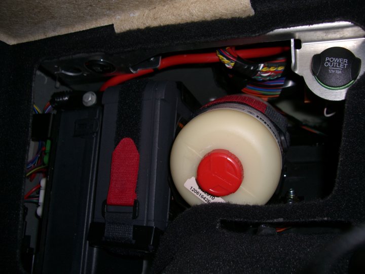 Vantage V8 Battery conditioner - Page 1 - Aston Martin - PistonHeads - The image shows a complex tangle of wires within the interior of a vehicle. A red cap around a red button, which could be a safety feature, is also visible. It seems to be taken in a darkened environment, possibly the car's trunk, and there is a label with the number 1256 on it. The wires are of varied sizes and seem to be interconnected in a somewhat chaotic manner.