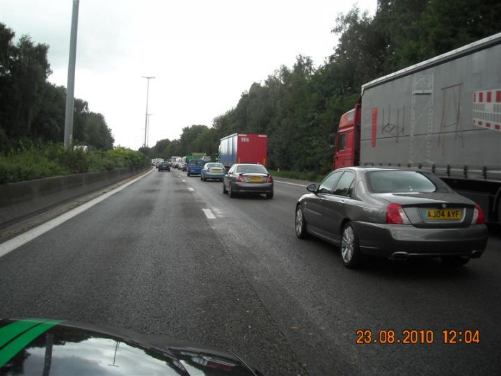 Pistonheads - The image depicts a busy highway filled with various types of vehicles, including cars and trucks. Traffic is heavy, with numerous cars closely following one another and a line of trucks at the back. The lanes are densely packed, suggesting a peak travel time, possibly during rush hour. The sky is overcast, and the setting appears to be either early morning or during a time of heavy traffic due to conditions on the route itself.