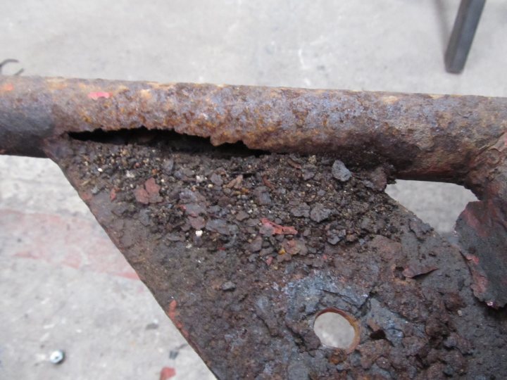 Pistonheads - The image shows a close-up of rusted metal, likely as part of a larger item such as a rail or bar. The focus is on the texture and color variation of the rust, indicating weathering and corrosion over time. There is a visible hole in the metal, which suggests wear or damage. The surrounding concrete floor has some PEX piping, which is a white, flexible conductive material, contrasting with the dark, rusted metal. The image evokes the experience of metal objects exposed to harsh environmental conditions.