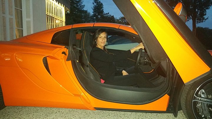 Car and Guitar solo road trip. - Page 3 - General Gassing - PistonHeads - In the image, a woman is seated in the driver's seat of a striking orange and black sports car. The car's futuristic design and Black interior contribute to its sleek and modern appearance. The woman, who is positioned centrally in the frame, is captured in a relaxed manner, perhaps preparing to drive. The scene takes place at night, with a house visible in the background and a glimpse of the night sky.