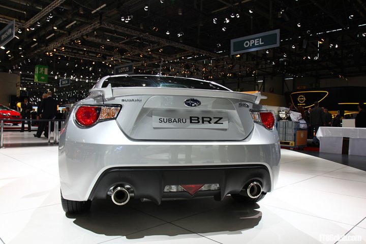 Pistonheads - The image showcases a white Subaru BRZ sports car resting on a white showroom floor. It's a side-angle shot with a focus on the back of the vehicle. The car is equipped with a rear spoiler and a dual exhaust pipe. 

The Subaru BRZ is prominently displayed under the brand name sign, making it the centerpiece of the showroom. The showroom itself has high ceilings and a large open space, giving the car a prominent display. 

In the background, there are blurred figures of people walking around, indicating that the showroom is open and that there are visitors walking around and observing the cars on display. The atmosphere seems to be busy and lively, typical of a car show or exhibition where various models are presented.