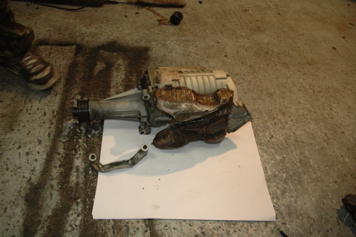 Leak Pistonheads Coolant - The image shows a dirty garage floor, where a significant amount of what appears to be oil has been spilled. At the center of the image, a lawn mower engine is placed on a sheet of paper. The lawn mower engine seems to be in poor condition, possibly having been part of a failed repair attempt. Its exposed components suggest it has been disassembled. The scene suggests someone has been working on the lawn mower engine, and it appears to be in need of replacement or overhaul due to the dirt and oil-soaked paper underneath it.