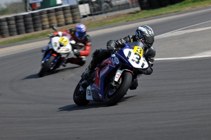 School Superbike California Pistonheads - The image captures an exhilarating scene on a motorcycle track. There are two motorcyclists racingHead-to-head, their helmets gleaming under the stadium lights. The motorcycle in the foreground is a striking blue, adorned with a bold red and white number "13". The other motorcycle is a bit behind, but still in the race. Both riders are leaning into the turn, a testament to their skill and the power of the machinery they command. The background reveals a vast, open sky, with the faint outlines of trees and a stadium. The image is a dynamic snapshot of a thrilling race.