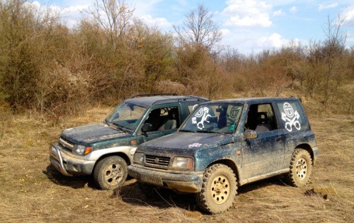 Pistonheads - The image shows two vehicles parked in a natural environment. Both vehicles appear to be old and dirty, suggesting they may have been used off-road or during rough conditions. The surroundings consist of dry grass and sparse vegetation, along with leafless trees indicating either a late season or a dry climate. There are no people visible in the photo. The vehicles are positioned side by side, extended into the frame, which creates a sense of depth and space in the image.