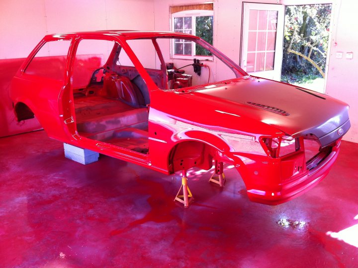 Fiesta RS Turbo Restoration - Page 7 - Ford - PistonHeads - The image shows a garage work in progress, where an older model red sports car is up on a car lift or system to allow work on the lower part near the ground. The interior of the car is visible through one of the open doors. The red sports car appears to be upside down for either maintenance or a paint job, indicating a professional car modification or restoration process. The garage is equipped with a large window on the right side, allowing natural light to enter. There is a view into the background that shows another part of the garage or workshop.