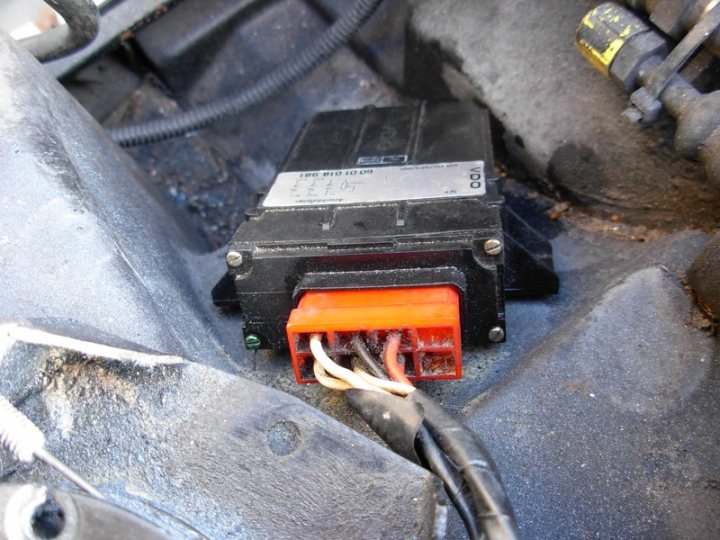 A pile of luggage sitting on the ground - The image is a side view of a vehicle's engine compartment. In the center, there is a black rectangular object, possibly a power or control relay. The relay is connected to a power source, indicated by a visible wire, which appears to be attached to a battery or a similar battery-like design. The object is surrounded by various black components that resemble brackets or mechanical parts, typical of a vehicle's engine bay. The background features a glimpse of the floor or a part of the vehicle's interior, but the focus is on the relay and its connections.