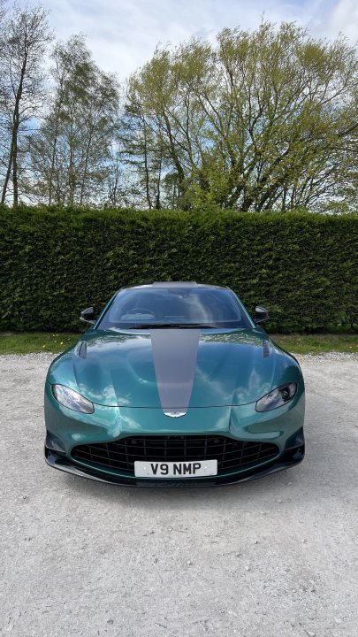 How about an Aston photo thread! - Page 222 - Aston Martin - PistonHeads UK - The image features a blue sports car, possibly an Aston Martin given the badge and design. It's parked in what appears to be a suburban driveway, with a neatly maintained lawn in the background. There is a clear sky above, suggesting it might be a nice day out. The vehicle has a large rear spoiler and a prominent front grille, typical of high-performance cars. The overall impression is that of a luxury car in an everyday setting.