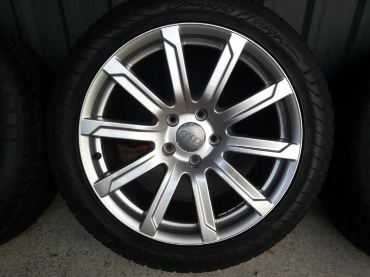 Q7 4.2 TDI - owner reviews and tips sought - Page 2 - Audi, VW, Seat & Skoda - PistonHeads - The image is a photograph of a single car wheel. The wheel has a silver metal finish with a multi-spoke wheel design. It appears to be mounted on a black tire. There are two nubs, likely lug nuts, visible through the spokes. The photograph is taken outdoors, likely in a garage or storage space, given the reflected light.