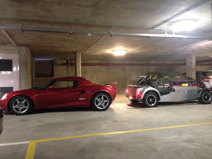 Me and my cars - Elise, Caterham and Integra R - Page 1 - Readers' Cars - PistonHeads - The image showcases a parking lot scene featuring two vehicles. On the left side of the frame is a vibrant red sports car, parked parallel to a concrete wall, showcasing its sleek design. On the right, a silver luxury car, with a distinctly long wheelbase, is parked in an adjacent space, reflecting its luxurious nature. The lighting suggests an indoor or enclosed parking structure, possibly situated below a ramp or high driveway. This could be a garage or an indoor parking building. The presence of yellow lines on the ground indicates designated spaces or parking rules, common in such structures. The text in the image mentions "ISO 497," which may refer to a standard related to vehicle tracking or parking procedures.