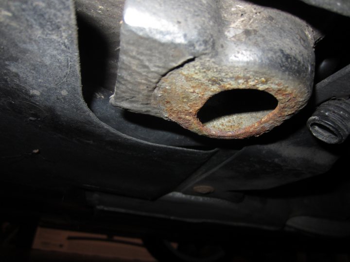 Do I need rubber pads to jack up my car? - Page 2 - Home Mechanics - PistonHeads - The image shows a close-up view of the underside of a car. A rusted metal part, possibly the exhaust or suspension system, is visible. There's an exposed bolt and a rusty part that has been painted. The background is dark with the focus on the rusty area. It appears to be taken in a garage or under a car, as indicated by the shadowing the underside.