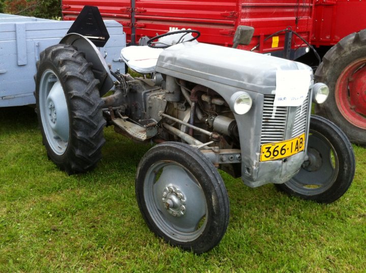 Classic tractors - Page 3 - Classic Cars and Yesterday's Heroes - PistonHeads - The image showcases a royal blue tractor parked on a grassy field with other farm equipment. The tractor, freshly painted, stands out with its white license plate that reads "366 AB." Its large tires provide a strong contrast to the lighter-colored parts of the vehicle. In the background, a vibrant red truck adds to the color palette of the image while parked in the field. The overall setting suggests a rural landscape, perhaps a farm or agricultural area.