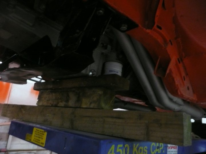 MK2 Escort LS1 in orange! - Page 3 - Readers' Cars - PistonHeads - This image shows a stack of heavy wooden boards against a white background. There's a hint of natural light illuminating the wood, giving it a warm tint. Two blue suspenders, more like cords, are attached to the wooden stack, possibly for lifting or hoisting purposes. The style of the picture is candid and utilitarian, capturing a practical moment in a workshop or garage setting.