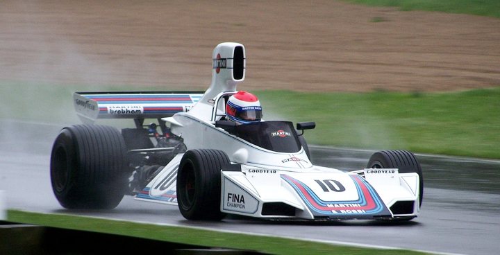 Fantastic Motorsport Pistonheads - In the image, a professional car racing event appears to be taking place. The main subject is a Formula One car, painted in a vibrant mix of blue and white, racing round a track. The car is in motion, suggesting high speeds, and is emitting a spray of water, which, given the sun in the top right corner, could indicate recent rain on the circuit. The driver, wearing a red and white striped helmet, is focused on the racing line, showcasing the intense concentration required in such high-stakes events. The black side mirrors, presumably filled with the stops and starts of the race, contrast with the colorful body of the car, offering a glimpse into the sport's competitive lifestyle.