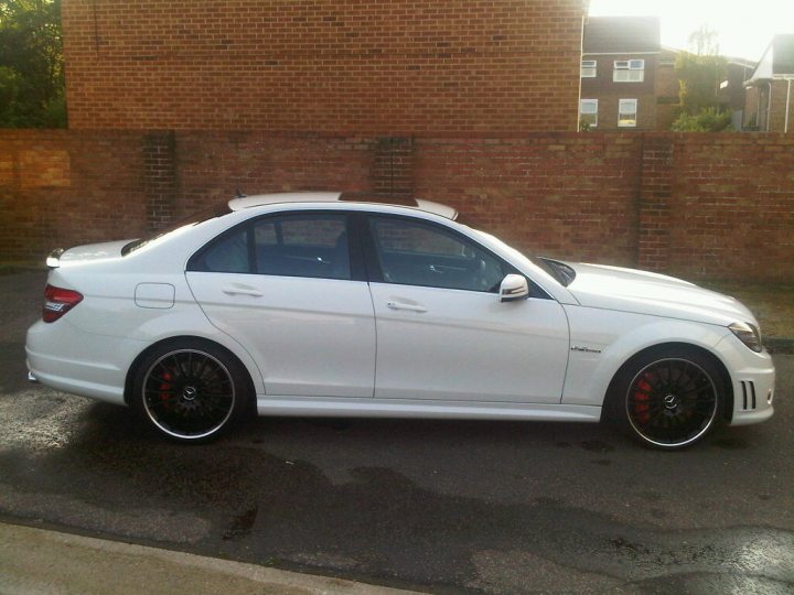 Any Photoshop experts in the house? - Page 2 - East Anglia - PistonHeads - The image shows a white BMW car parked on the street. The car is facing towards the right side of the image, and it is positioned close to a red brick wall. The vehicle appears to be equipped with alloy wheels, and there's evidence of recent rain, as some water from the puddles surrounding the area where the car is parked is visible on the ground. There are no people or other vehicles in view, giving the scene an undisturbed and serene ambiance. The car itself looks to be well-maintained and in good condition.